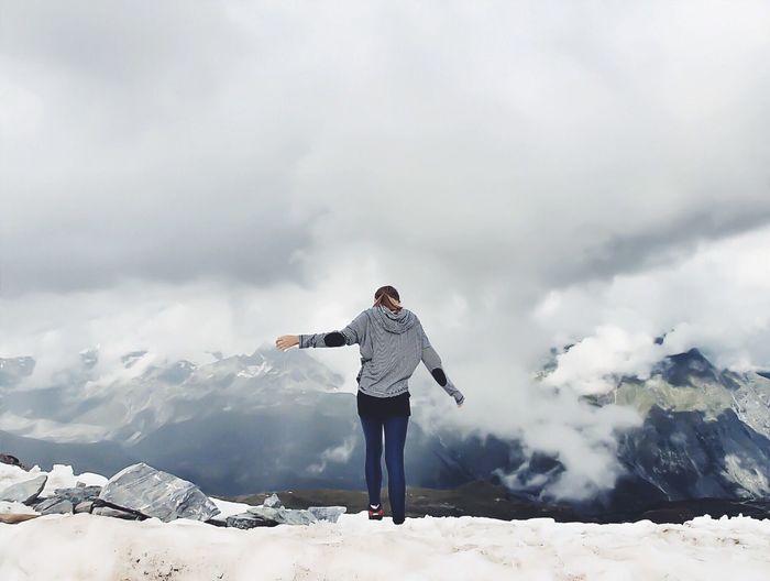 Rear view of woman standing on snowcapped mountain against cloudy sky