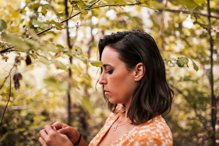 Thoughtful woman standing amidst trees in forest