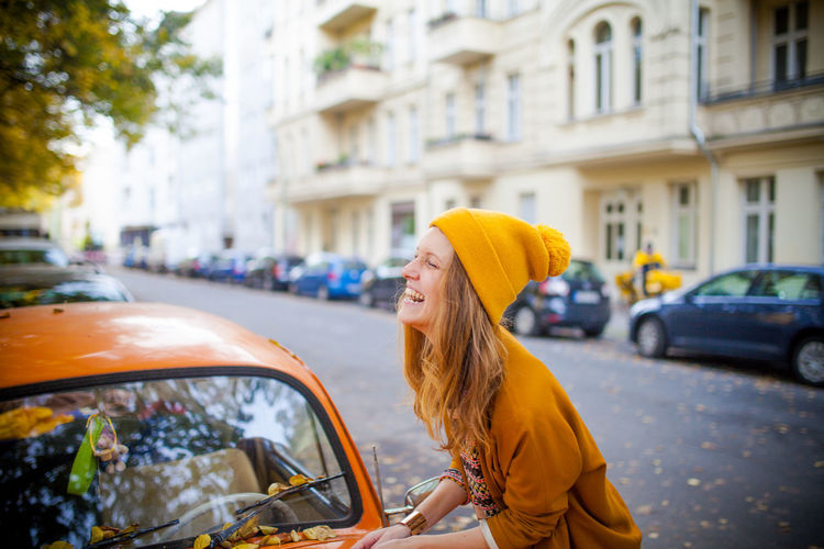 Side view of smiling young woman by car on street
