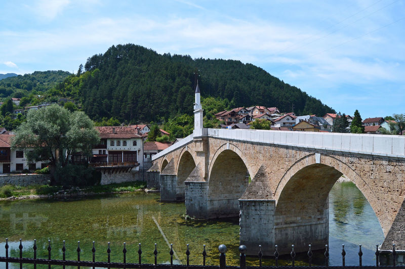 Arch bridge over river by buildings against sky