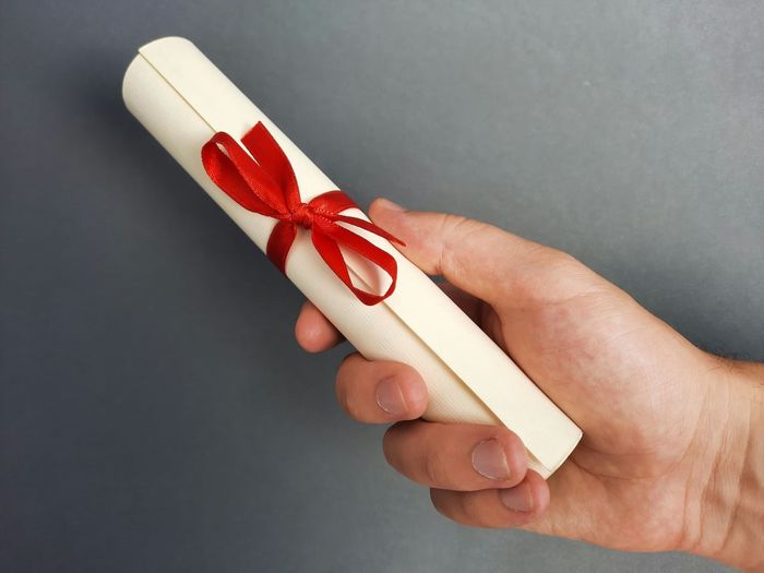 Close-up of hand holding red paper over white background