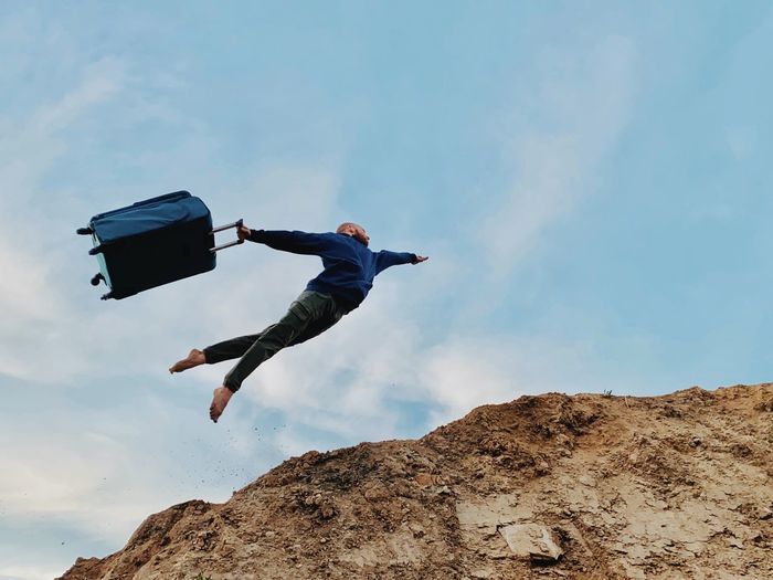 low angle view of man jumping on mountain against sky