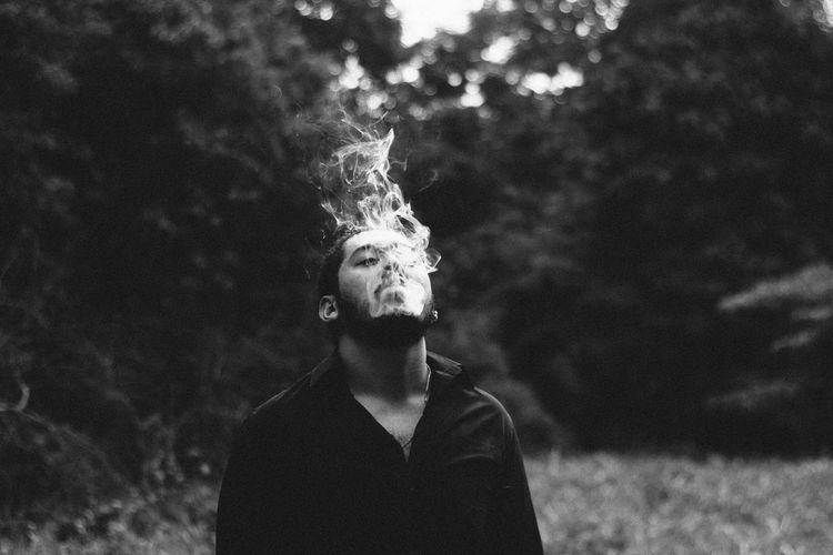 Close-up of man smoking against trees