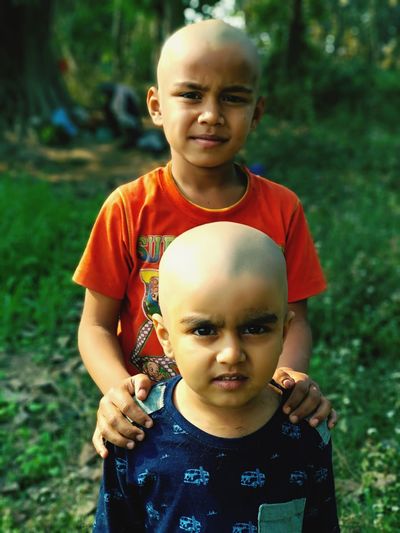 Portrait of cute brothers with shaved head standing on field