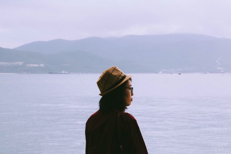 Woman in hat looking at sea against mountains 