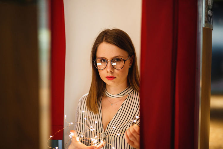 Portrait of woman holding illuminated string lights while standing against wall