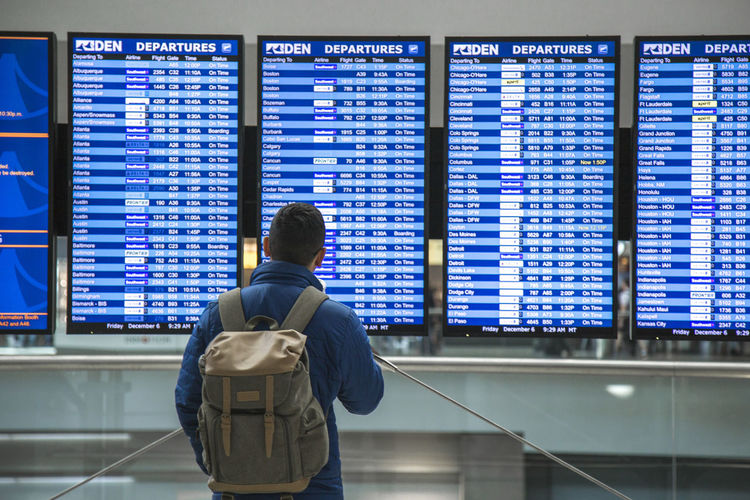 Rear view of man looking at flight times at an airport 