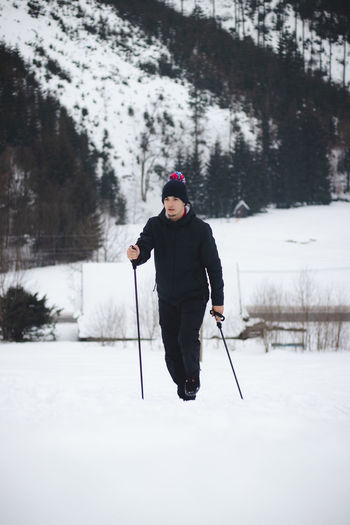 Man in winter clothes climbs ski slope to the top with  help of climbing poles for better stability