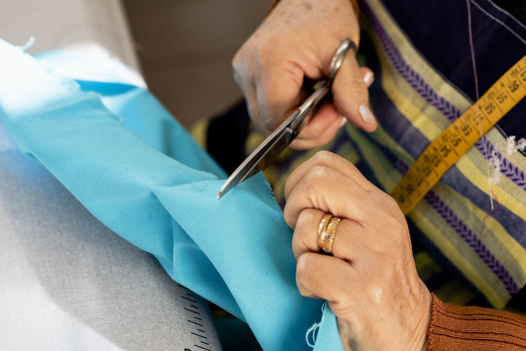 Detail of senior dressmaker hands cutting fabric with scissors.