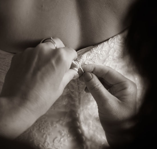 Cropped hands of woman dressing bride during wedding ceremony