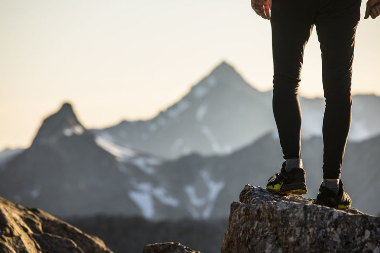 View of trail runners legs and shoes perched on a mountain summit.