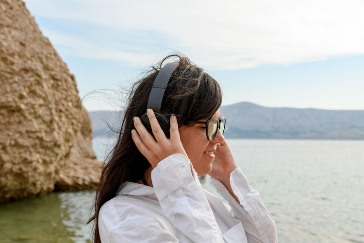 Beautiful young woman standing on beach listening to music on headphones.