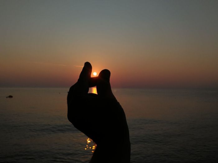 Silhouette hand on beach against sky during sunset