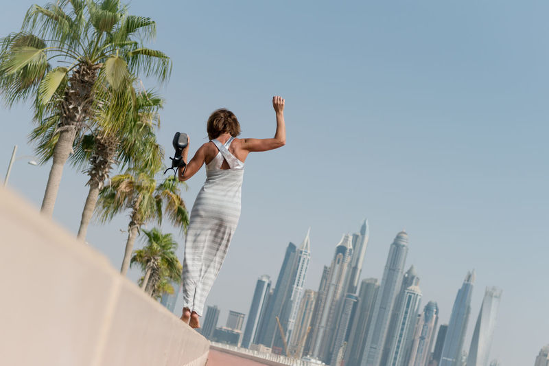 Rear view of woman standing by palm trees against clear sky