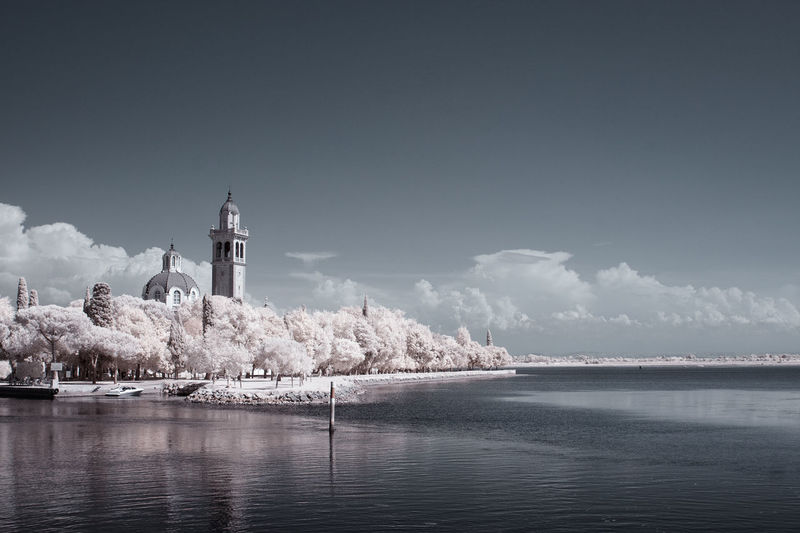 Church with trees by sea against sky