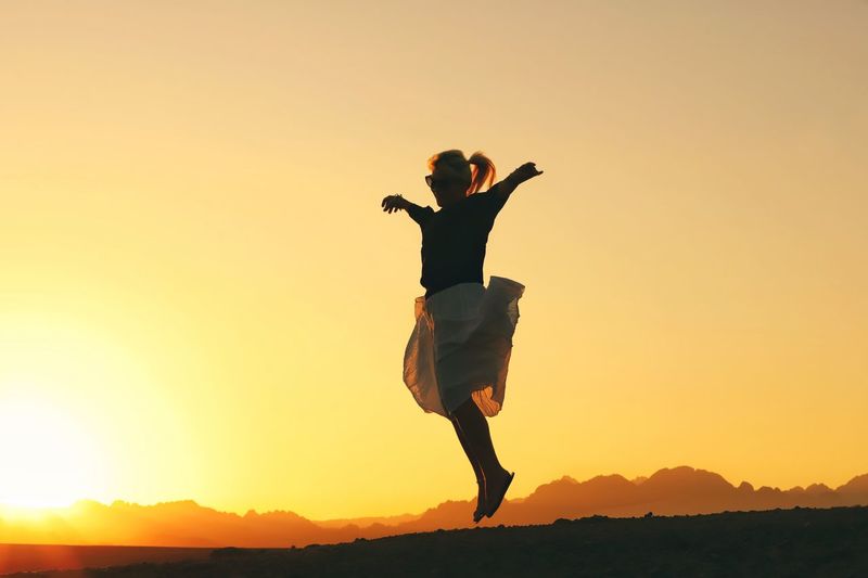 Full length of silhouette woman jumping against clear orange sky