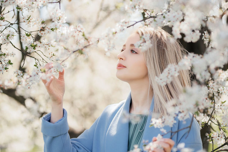 Portrait of young woman standing against cherry blossom