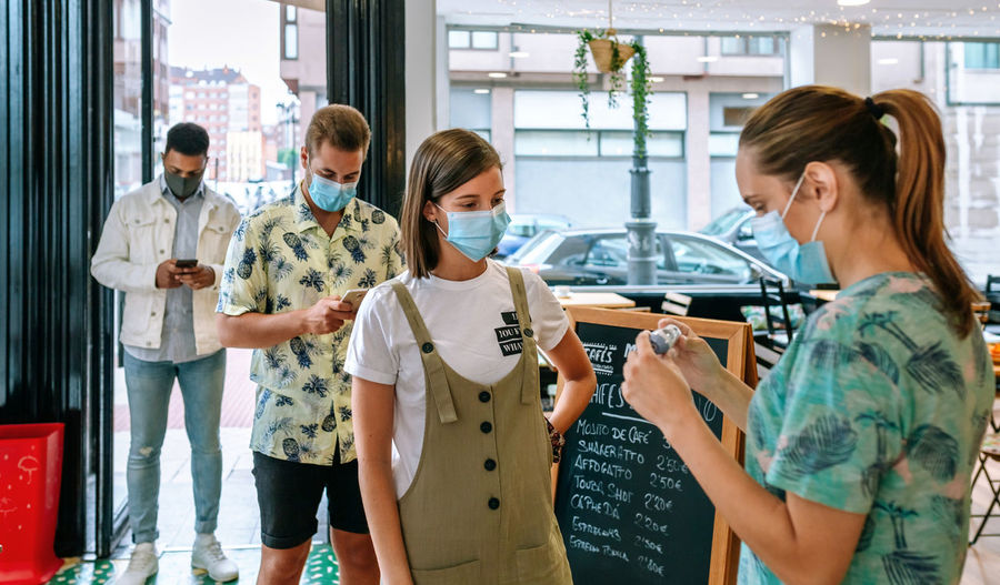 Woman checking temperature of customers wearing mask in restaurant