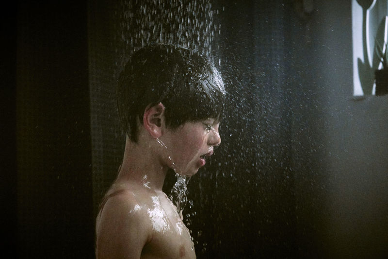 Side view of shirtless boy showering in bathroom