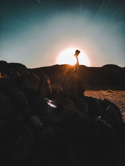 Man standing on rock against sky during sunset