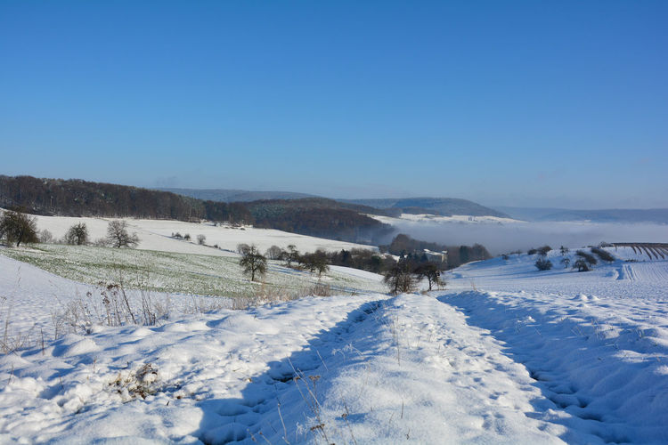 Winter landscape with fields and fog in the valley, with snow, blue sky, germany, bavaria, spessart