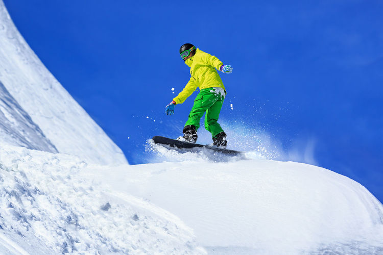 Full length of man snowboarding on snowcapped mountain against blue sky