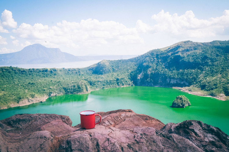 Mug on rock by lake and mountain against sky