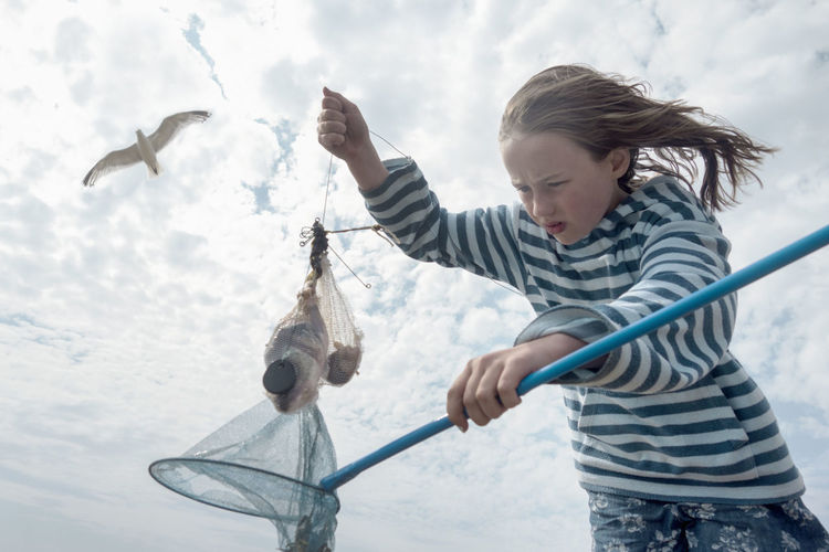 Girl catching crab in fishing net against cloudy sky