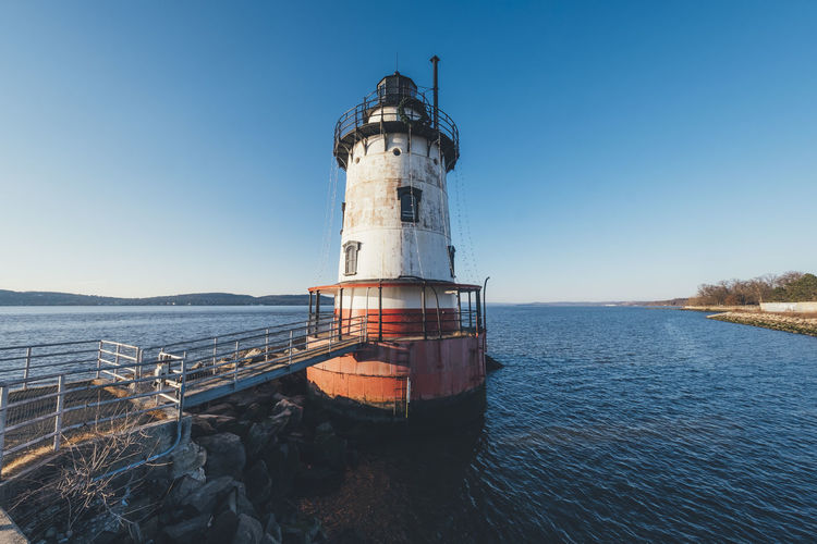 Lighthouse in sea against clear blue sky
