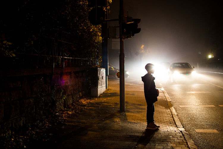 Side view of boy standing on footpath at night