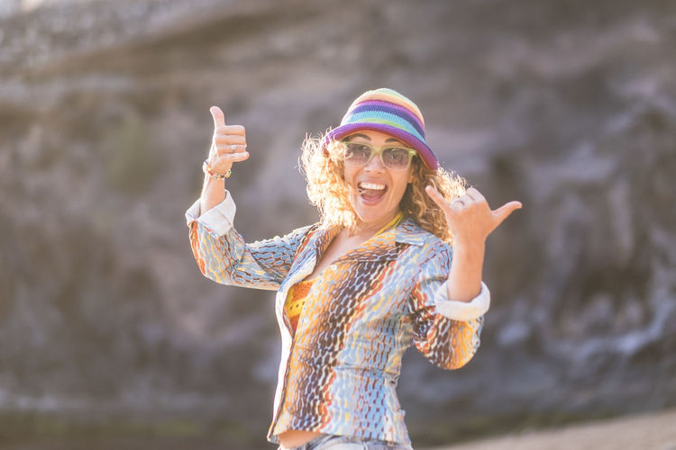 Cheerful woman wearing hat standing against rock formation