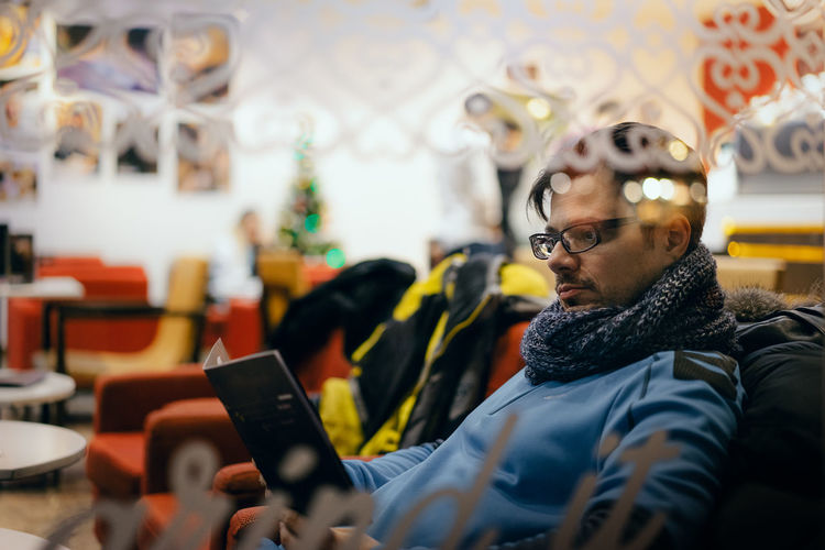 Mid adult man using digital tablet seen through glass window at restaurant