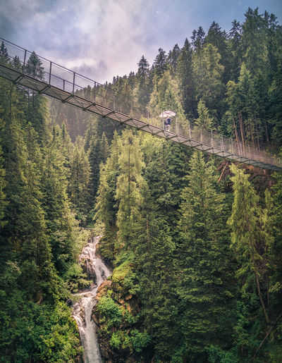 Person trekking footbridge in mountain scenery
