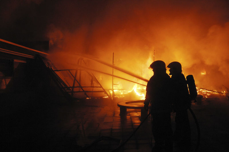 Silhouette firefighters working in city against sky at night