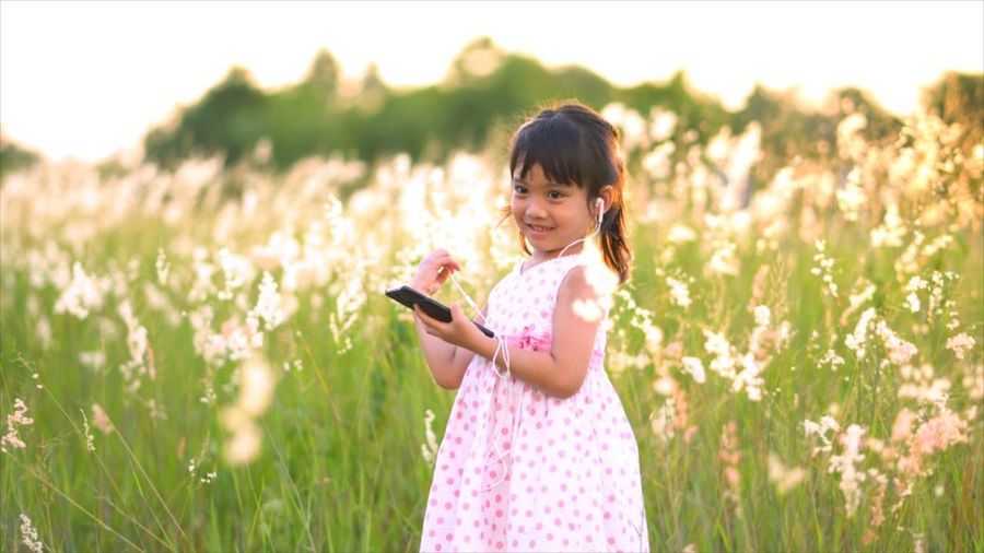 Smiling girl listening to music while standing against plants