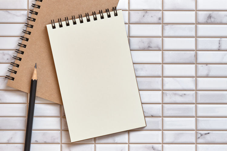 Open blank notebook and pencil on white tile background, copy space for text, top table view.