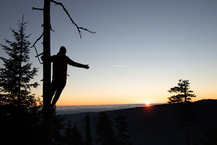 Silhouette man with arms raised against sky during sunset