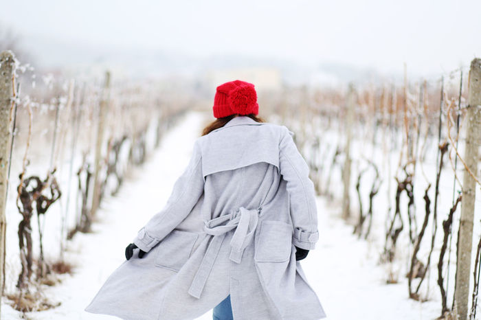 REAR VIEW OF WOMAN ON SNOW COVERED FIELD AGAINST SKY
