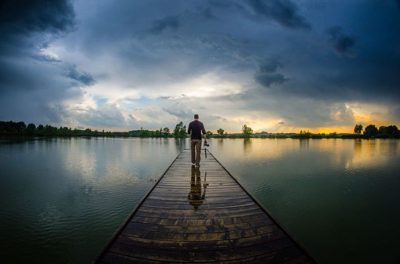 Man standing on jetty by lake against sky