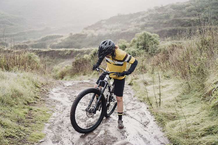Full body of female cyclist on muddy mountain path on rainy day