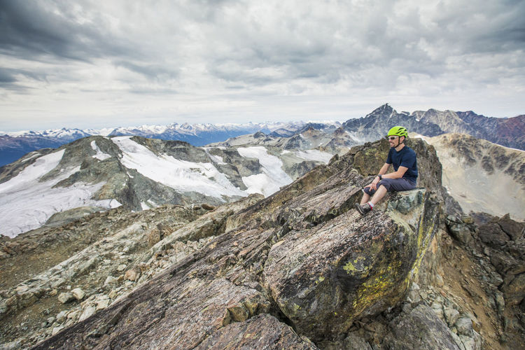 Climber sits on the rocky summit of a mountain.