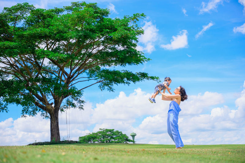 Woman standing by tree on field against sky