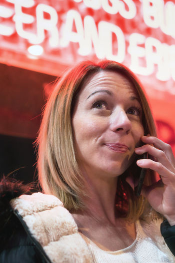 Close-up of woman talking on smart phone against illuminated shop