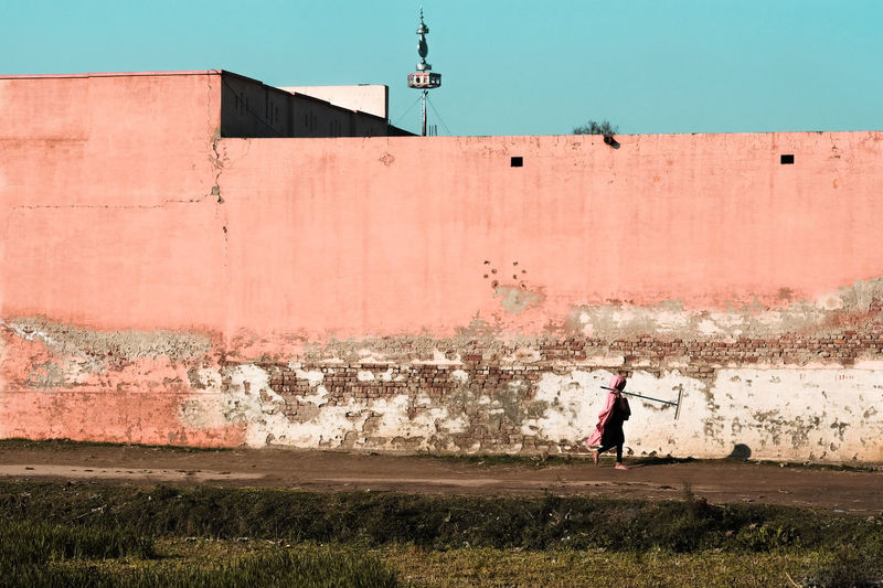 Woman walking against wall and sky in city