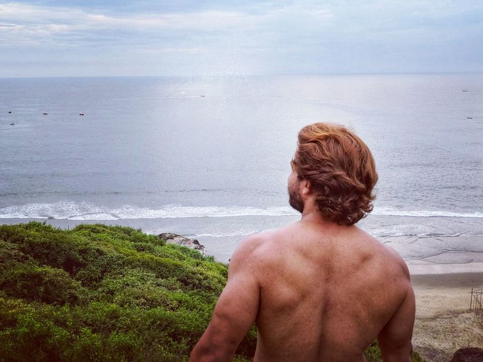Rear view of shirtless man standing against sea