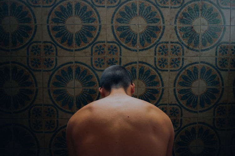 Rear view of shirtless man by tiled wall