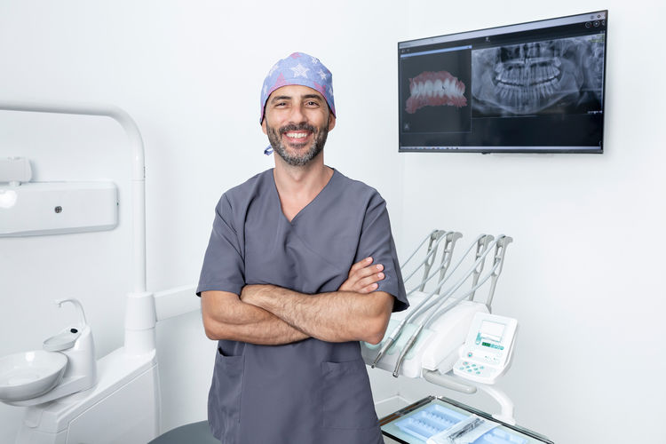 Portrait of a dentist in uniform and protective cap standing with arms crossed in a dental clinic
