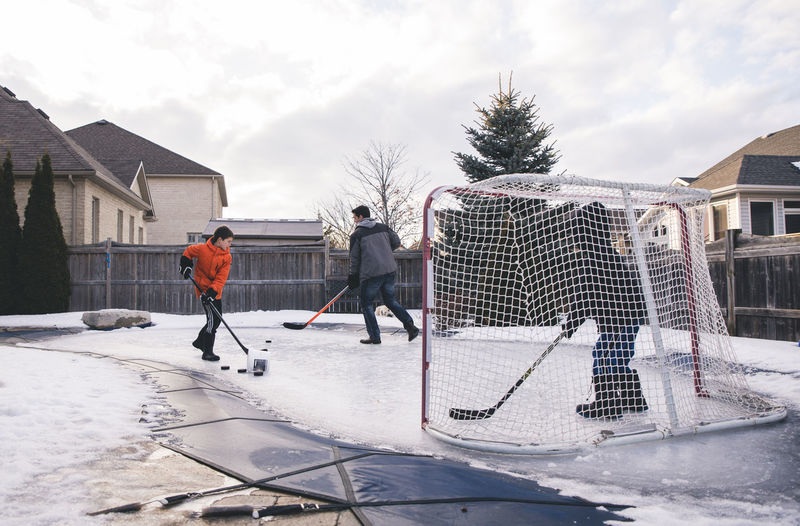 Father with sons playing ice hockey at yard against sky