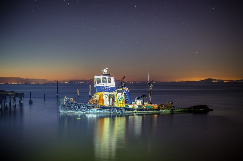 Tugboat on calm sea against sky at dusk