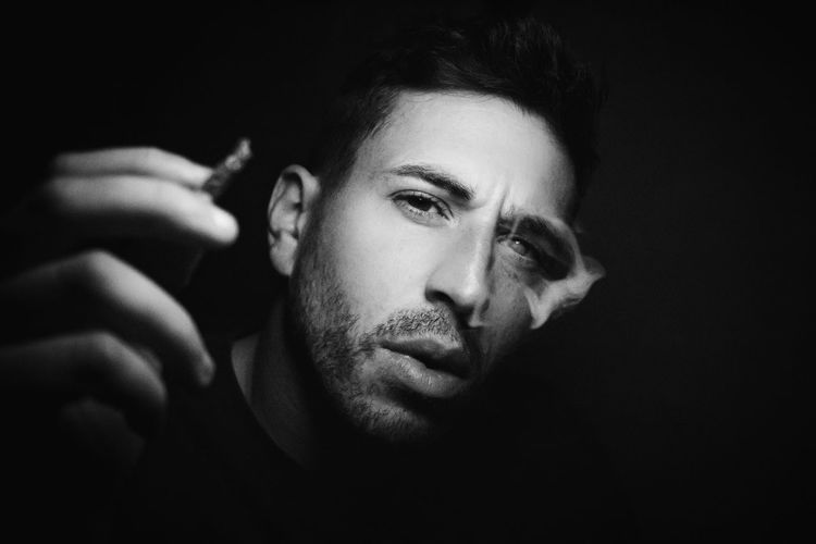 Close-up portrait of young man smoking joint against black background